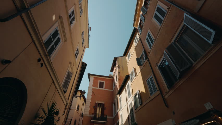 Narrow Roman street with warm-colored buildings and open shutters creating a picturesque upward perspective view. High quality 4k footage