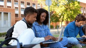 Young diverse couple of university students happily studying and sharing a laptop computer while sitting on the green grass of the college campus, smiling and having fun with their friends - Powered by Shutterstock - Get 15% off with code: PIKWIZARD15