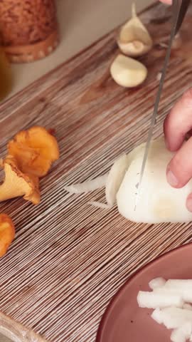 Anonymous person cut onion with knife on wooden board. Healthy eating and cooking at home. Vegan, cholesterol-free, and gluten-free.