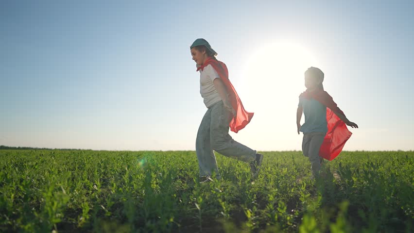 Girl smiling running on open field. Boy follows playing superhero adventure. Kid waving arms like flying. Outdoor summer day child running superhero. Boy laughing with girl on field playing joy.