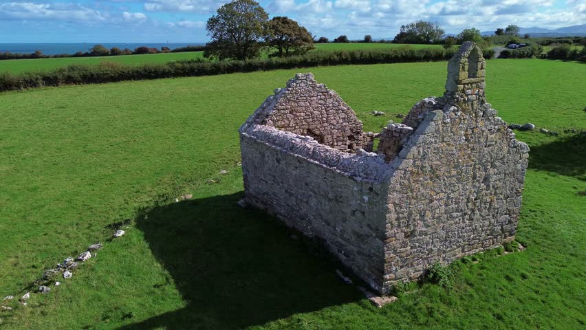Lligwy chapel aerial view slow circling lush meadow farmland medieval churchyard ruins close up