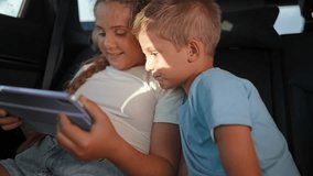Boy and girl using tablet in backseat of moving car while watching screen together. Siblings quietly entertained during trip. Children enjoy digital content. Kids focus on screen while riding - Powered by Shutterstock - Get 15% off with code: PIKWIZARD15