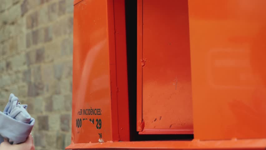 Woman donates clothes at orange bins used items into a charity container in Spain. Concept of helping people in need and supporting.
