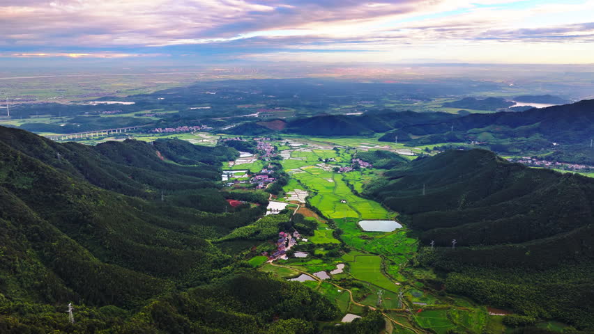 Aerial shot of beautiful green rice fields and rural villages nestled in a valley surrounded by mountains at sunrise 