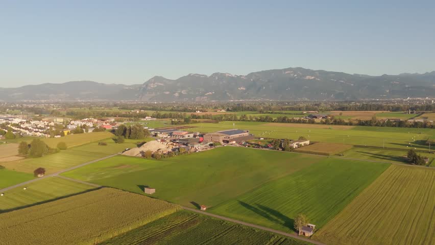 Fields and farms fill a Swiss valley below alpine foothills; forward drone approach.