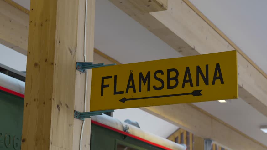 Interior shot from Flåm Railway Museum, Norway, featuring FLÅMSBANA directional signage and vintage train car in a timber-framed station setting.