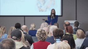 Engaged audience participates in conference session, raising hands to answer questions as presenter speaks at front with projector screen displaying slides - Powered by Shutterstock - Get 15% off with code: PIKWIZARD15