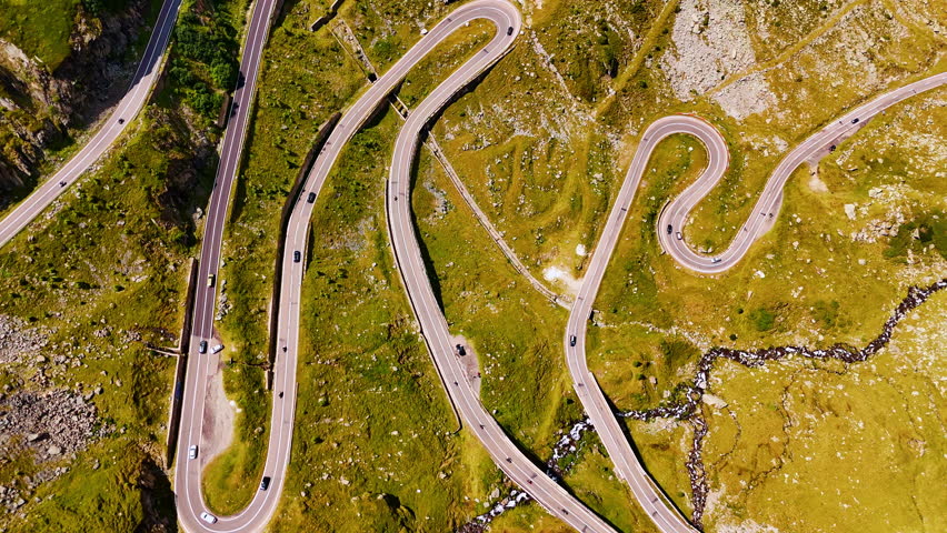 Amazing view on the valley crossed by the wavy road. Cars run by the Transfagarash highway in Romania. Aerial view.
