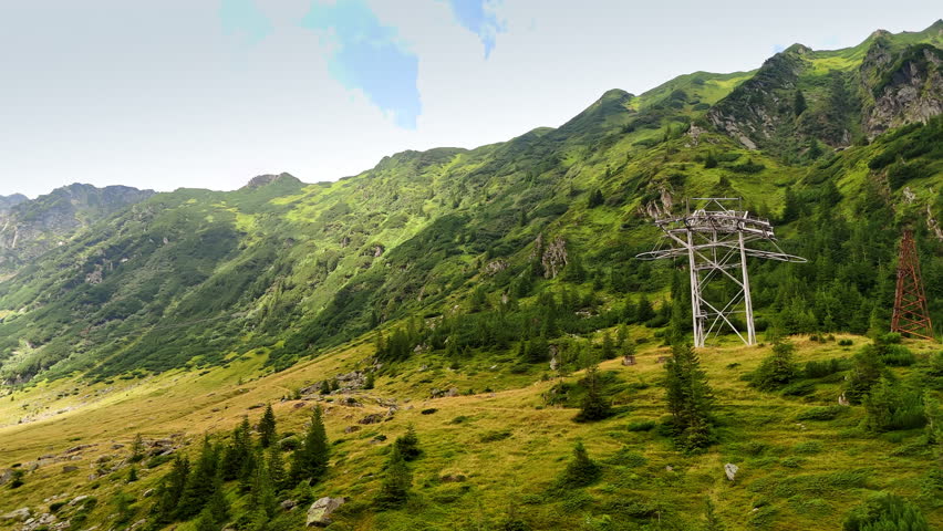 Power line supports installed in the green mountains. Lovely pine trees grow on the slopes. Nature of Romania. Aerial view.
