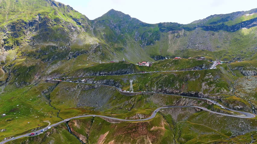 Approaching the picturesque slopes of the mountains with a highway. Multiple cars stand on the highway. Famous Transfagarash highway in Romania.