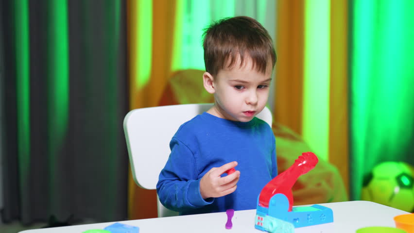 Toddler boy in blue sweater plays with molding machine. Happy kid absorbed by the game.