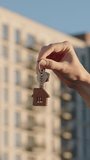 Vertical close up of female real estate owner handing over house key with home shaped keychain to young man in front of modern apartment building. Both are satisfied, first home and successful deal. - Powered by Shutterstock - Get 15% off with code: PIKWIZARD15