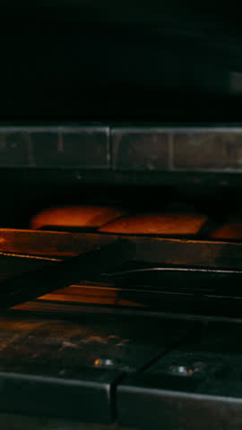 A baker takes bread out of the oven with a large wooden shovel, close-up. Bakery business. Baking bread and bakery products.