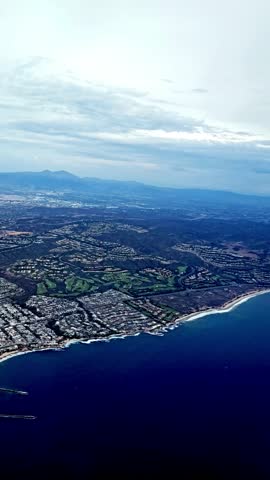 Airplane POV showing coastline with bright blue water meeting the land. Aerial perspective highlights the beauty of coastal travel and exploration.
