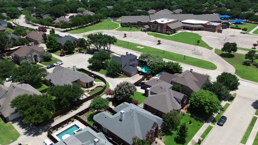 Upscale corner-lot homes in Coppell, Texas featuring shingle roofs, fenced yards, swimming pools, mature trees, Cottonwood Creek Elementary campus, circular driveway, shaded playground visible. USA