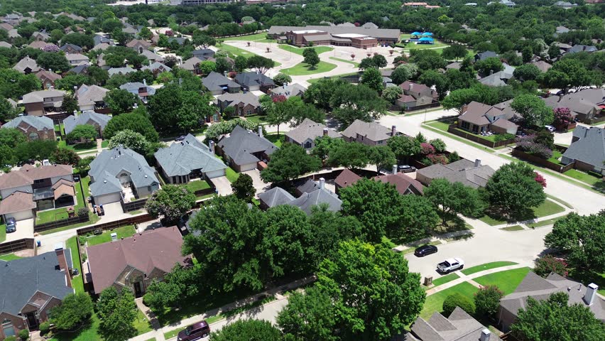 Large two-story homes in Coppell, Texas with fenced yards, mature trees, and solar panel rooftop, along quiet residential street leading to Cottonwood Creek Elementary and nearby commercial zone. USA