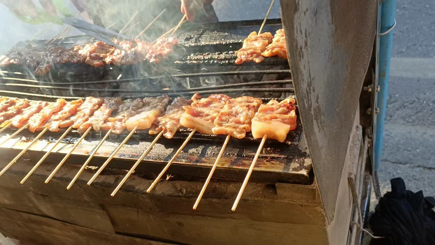 Grilled meat skewers charcoal grill with hand turning kebab and grilled chicken skewer with golden glaze, sizzling street food scene of outdoor charcoal grill, smoky aroma, char marks, warm