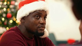 Portrait of an African man wearing a Santa hat during Christmas celebration. Warm holiday atmosphere with festive lights and Christmas tree background, Listening friend talking at the table - Powered by Shutterstock - Get 15% off with code: PIKWIZARD15