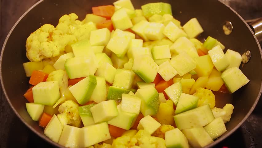 Frozen green beans are added to vegetable curry, covered with a lid and simmered on a hot stove
