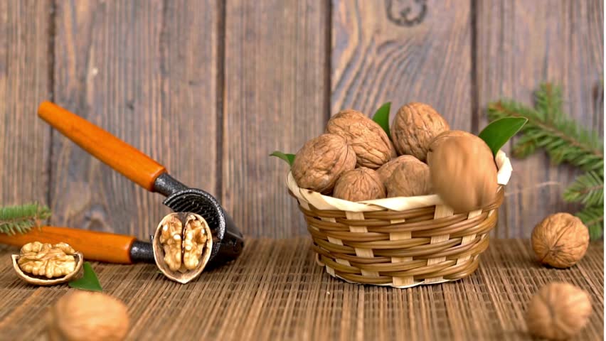 Walnuts Falling into a Woven Basket on a Rustic Wooden Table with Nutcracker, Healthy Holiday Snack Close-up