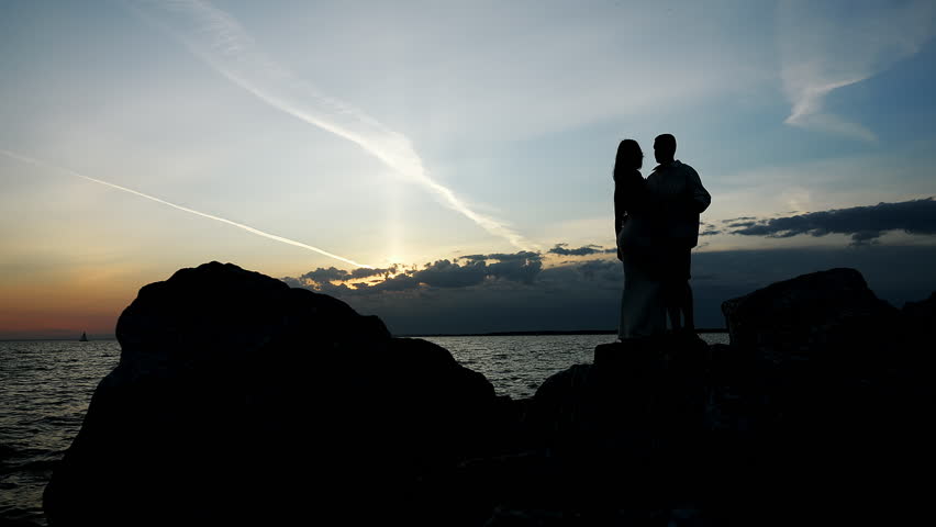 A silhouette of two people in love, a man and a woman, standing on the seashore at sunset. Family vacation on a tropical coast.