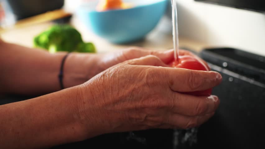 Hands are shown rinsing fresh vegetables under running water in a kitchen sink.