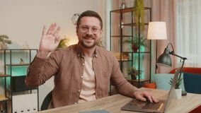 Hello. Happy Caucasian businessman employee waves hand hi gesture greeting welcomes someone, online webinar, remote distance conversation. Freelance guy sitting at desk using laptop in home office. - Powered by Shutterstock - Get 15% off with code: PIKWIZARD15