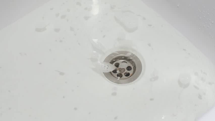 Bathroom sink drains water slowly with foam swirling around the metal grate, showing clog problem and need for plumbing maintenance.