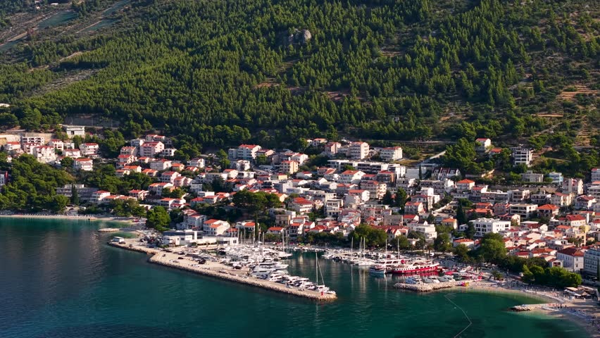 Stunning aerial view of Croatian coastal town with red roofed houses bustling marina and crystal clear turquoise waters surrounded by pine forests