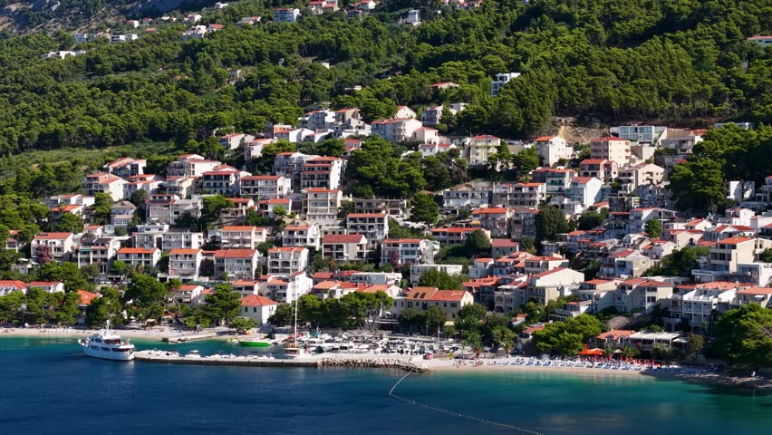 Stunning aerial view of Croatian coastal town with red tile roofs white buildings and small marina surrounded by dense Mediterranean forest