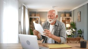 Elderly man sitting at a table with a laptop, opening an envelope and reading a document with great news, feeling overjoyed, celebrating his success, and clenching his fists in excitement - Powered by Shutterstock - Get 15% off with code: PIKWIZARD15