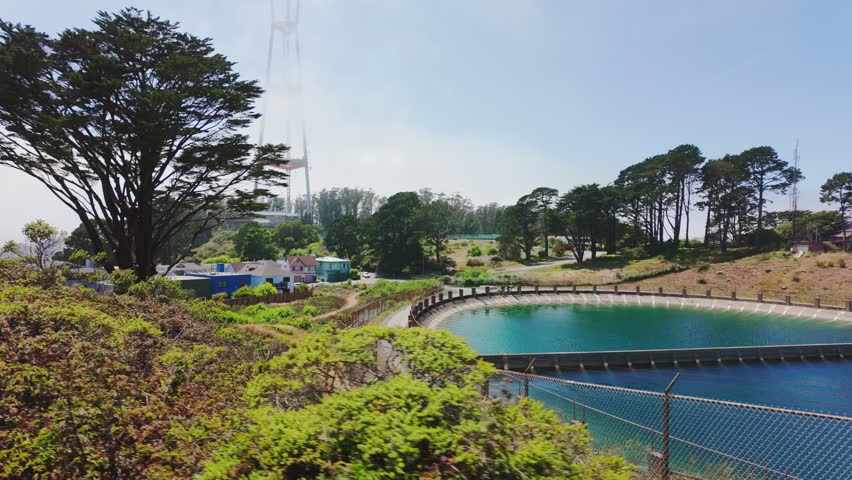 Twin Peaks Reservoir with turquoise water and Sutro Tower rising above trees in San Francisco, California, USA. Scenic urban landmark with greenery, hills and clear summer sky