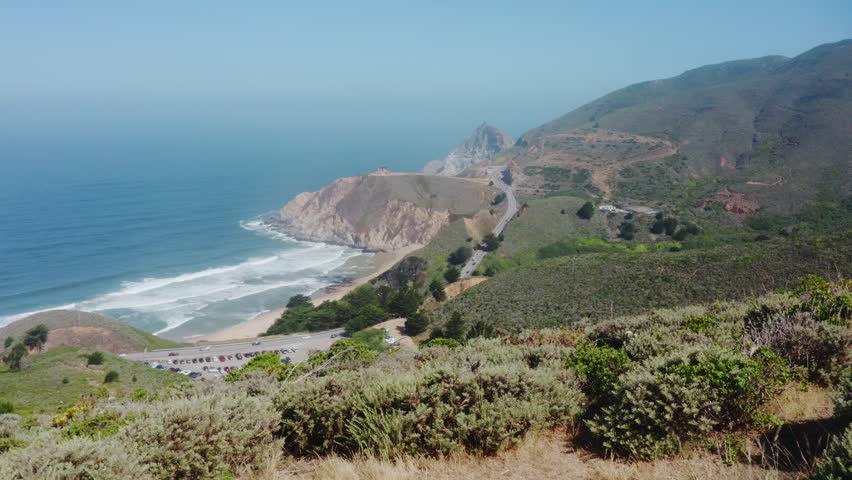 Scenic view from Green Valley Hiking Trail of rolling hills, Highway 1 and the Pacific Ocean coastline in California, USA. Coastal landscape with waves, beach and summer sky