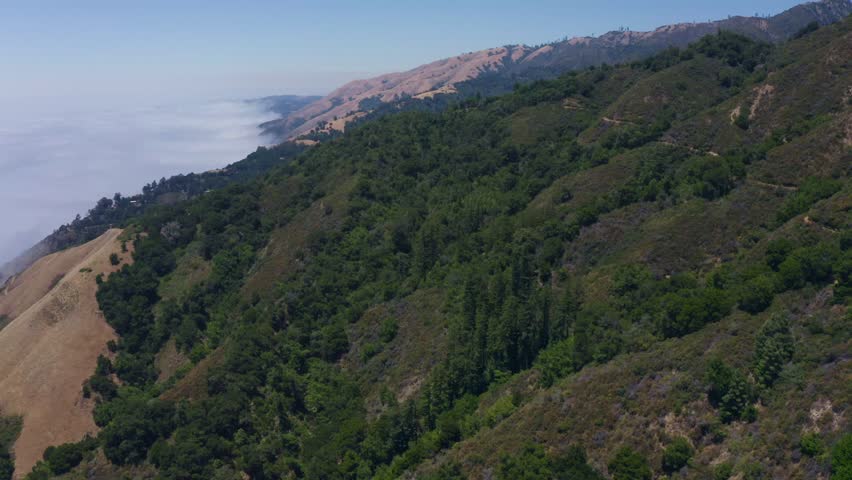 Big Sur California USA video footage of scenic mountain ridges covered with green forest and coastal fog rolling in from the Pacific Ocean along Highway 1, iconic landscape of Californias central
