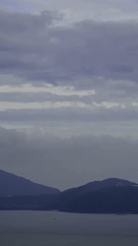 Dramatic cloudy sky over a serene bay with distant mountains and tranquil water, creating a peaceful and moody landscape.