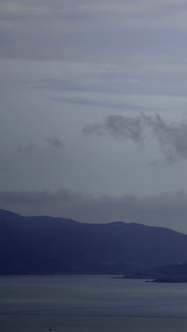 Serene landscape of dark mountains overlooking a tranquil bay under a soft, overcast sky with subtle clouds.
