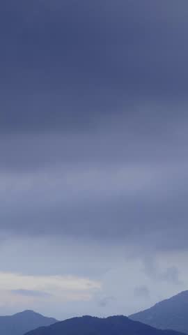 Expansive blue and grey sky with soft clouds and a subtle crescent moon over distant mountain silhouettes at twilight