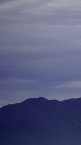 Dark mountain range silhouette under a vast, cloudy sky at twilight, showcasing a serene and dramatic natural landscape