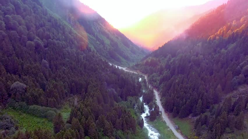 breathtaking aerial view of a mountain valley at sunset. a river winds through a lush forest, creating a stunning natural landscape. the perfect scenic getaway.