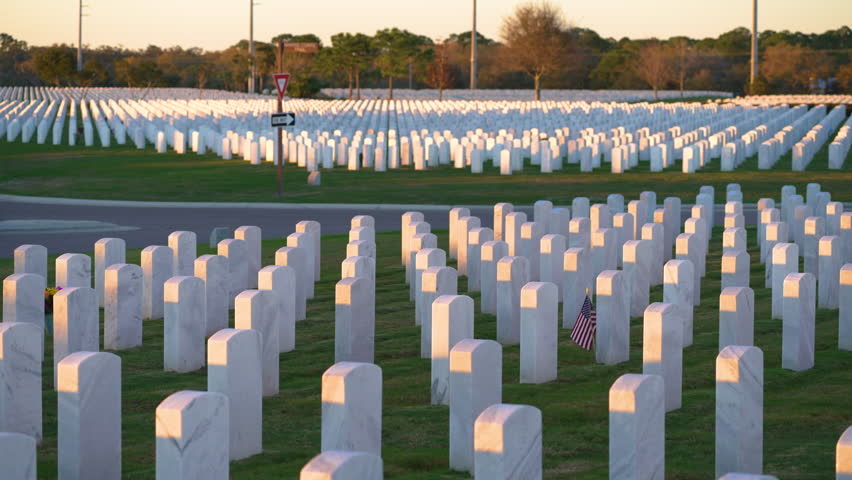 American army national cemetery with rows of white headstones and USA flag on green grass lawn. Memorial Day concept.