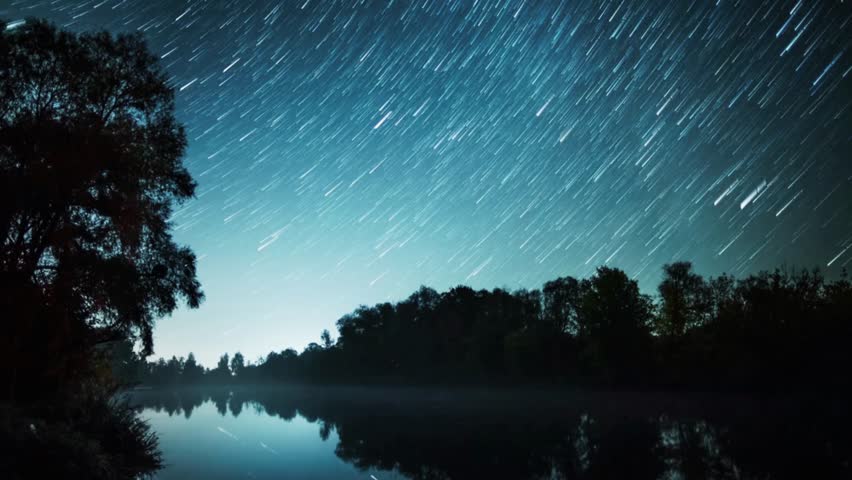 a beautiful time lapse of the night sky over a calm lake. the stars create stunning trails as they move across the sky. enjoy the beauty of nature and space together!
