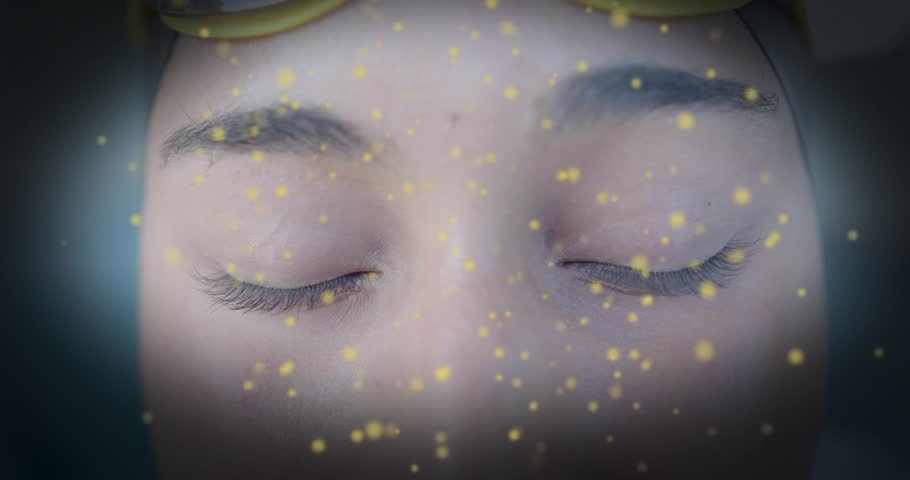 Woman wearing yellow-tinted goggles blinking to test AR eye tracking as golden particles swirl. Digital art, futuristic, immersive, technology, visionary, abstract, luxury