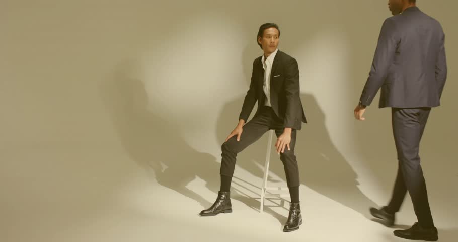 Fashion shoot models moving from seated to standing pose with stool after photographer signaling. Minimalist, introspective, sophisticated, monochrome, professional, dynamic, elegant