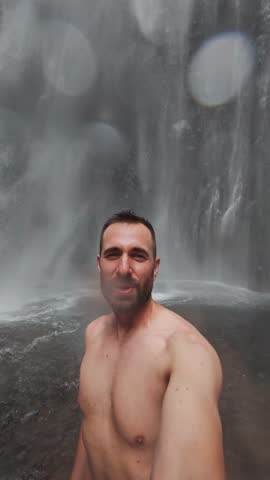 Adventurous man taking selfie under waterfall
