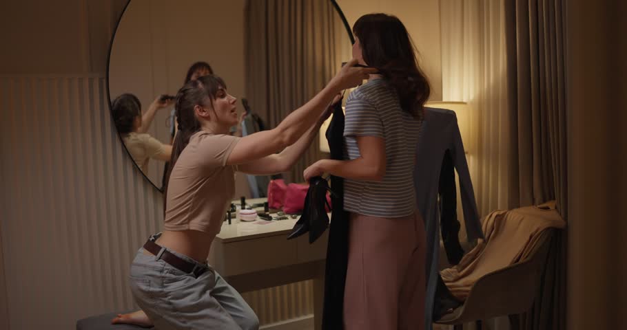 Two friends share tips and laughter while getting ready for a special night out in a chic hotel room