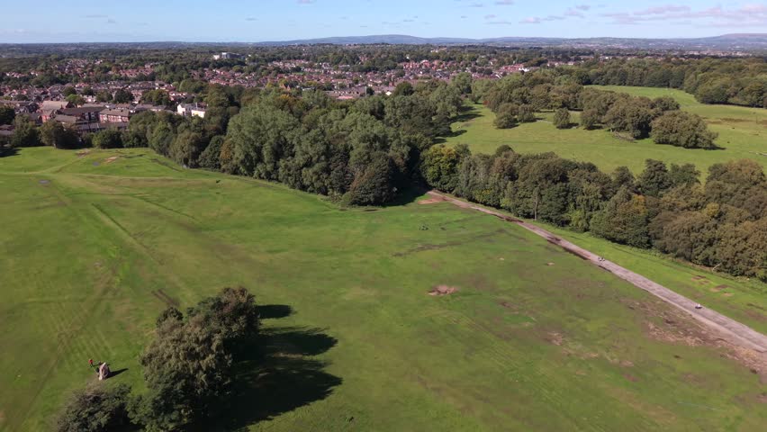 Aerial video of Heaton Park fields, woodland, and suburban Prestwich housing under a clear blue sky. Manchester - UK. 