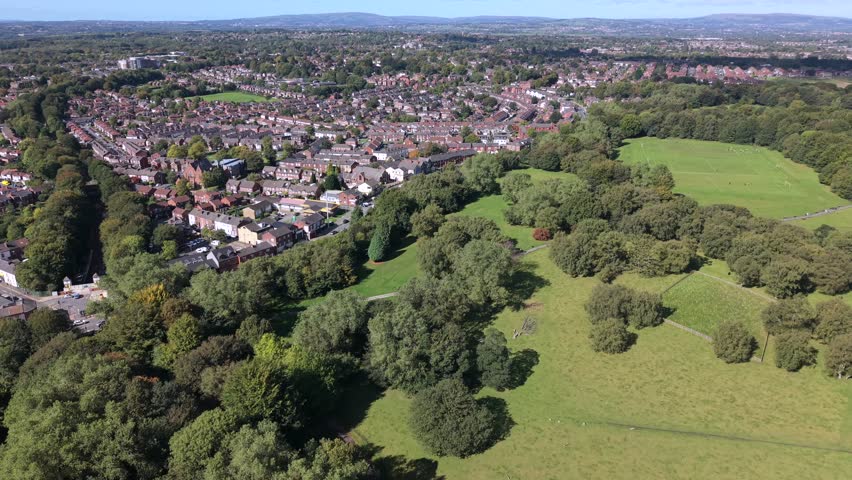 Aerial video of Heaton Park fields, woodland, and suburban Prestwich housing under a clear blue sky. Manchester - UK. 