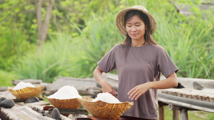 Portrait of young woman farmer with harvested natural sea salt in hands, bali, indonesia, farming, smiling, looking at camera, slow motion