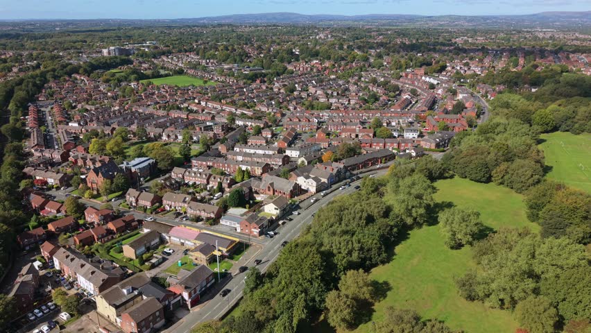 Aerial video of Heaton Park fields, woodland, and suburban Prestwich housing under a clear blue sky. Manchester - UK. 