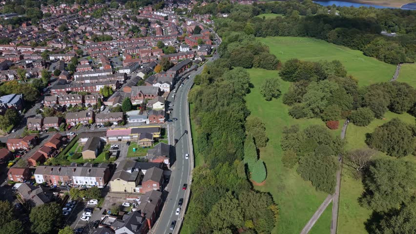 Aerial video of Heaton Park fields, woodland, and suburban Prestwich housing under a clear blue sky. Manchester - UK. 